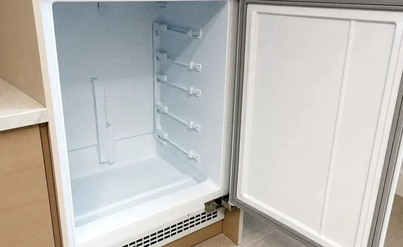 A white undercounter refrigeration cabinet with its door swung open on an empty interior and a vented grille at the base