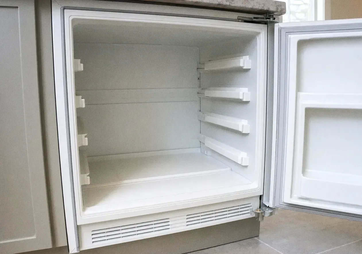 The empty white interior of a refrigeration cabinet with the door open wide and moulded shelf rails on both walls