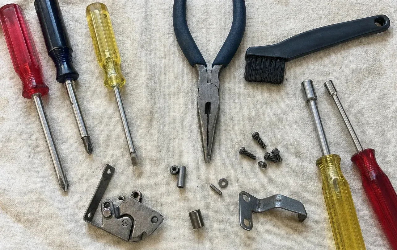 A screwdriver, long-nose pliers and a brush laid out with a hinge plate, roller pins, bolts and a small bracket